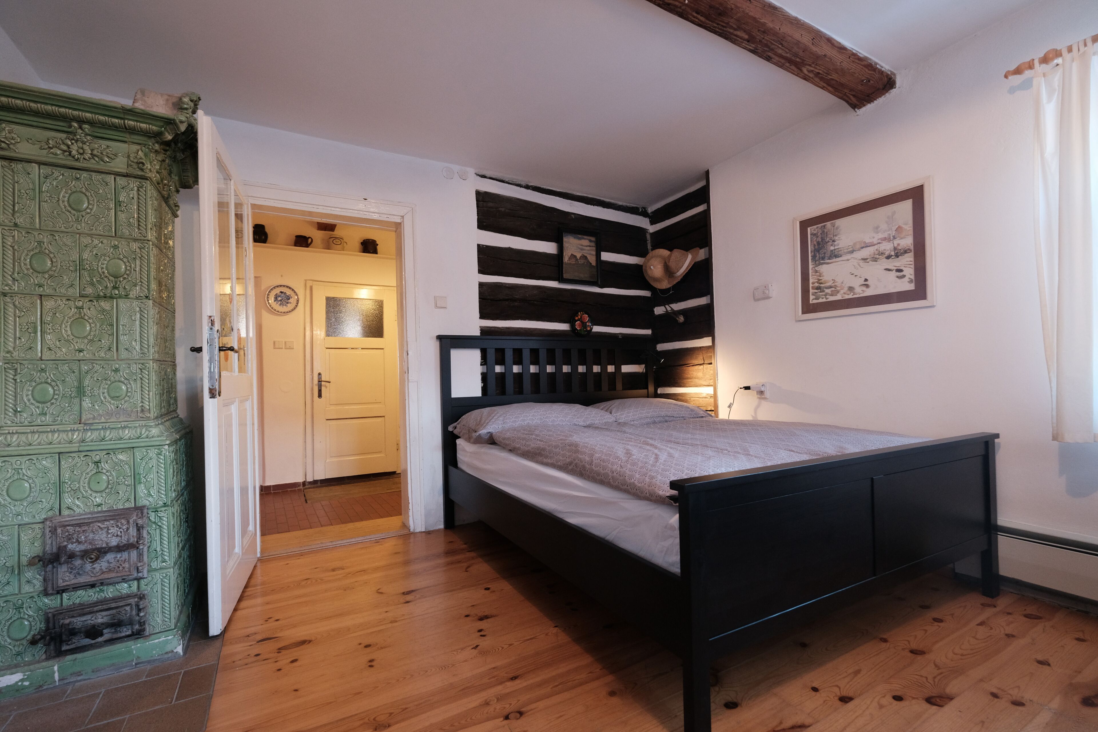 Un dormitorio con suelo de madera, estructura de cama negra, puerta verde y pared blanca con un cuadro.