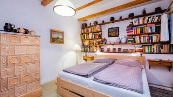 Un lit en bois avec deux oreillers, une table de chevet, une lampe et une bibliothèque remplie de livres et d’objets décoratifs.