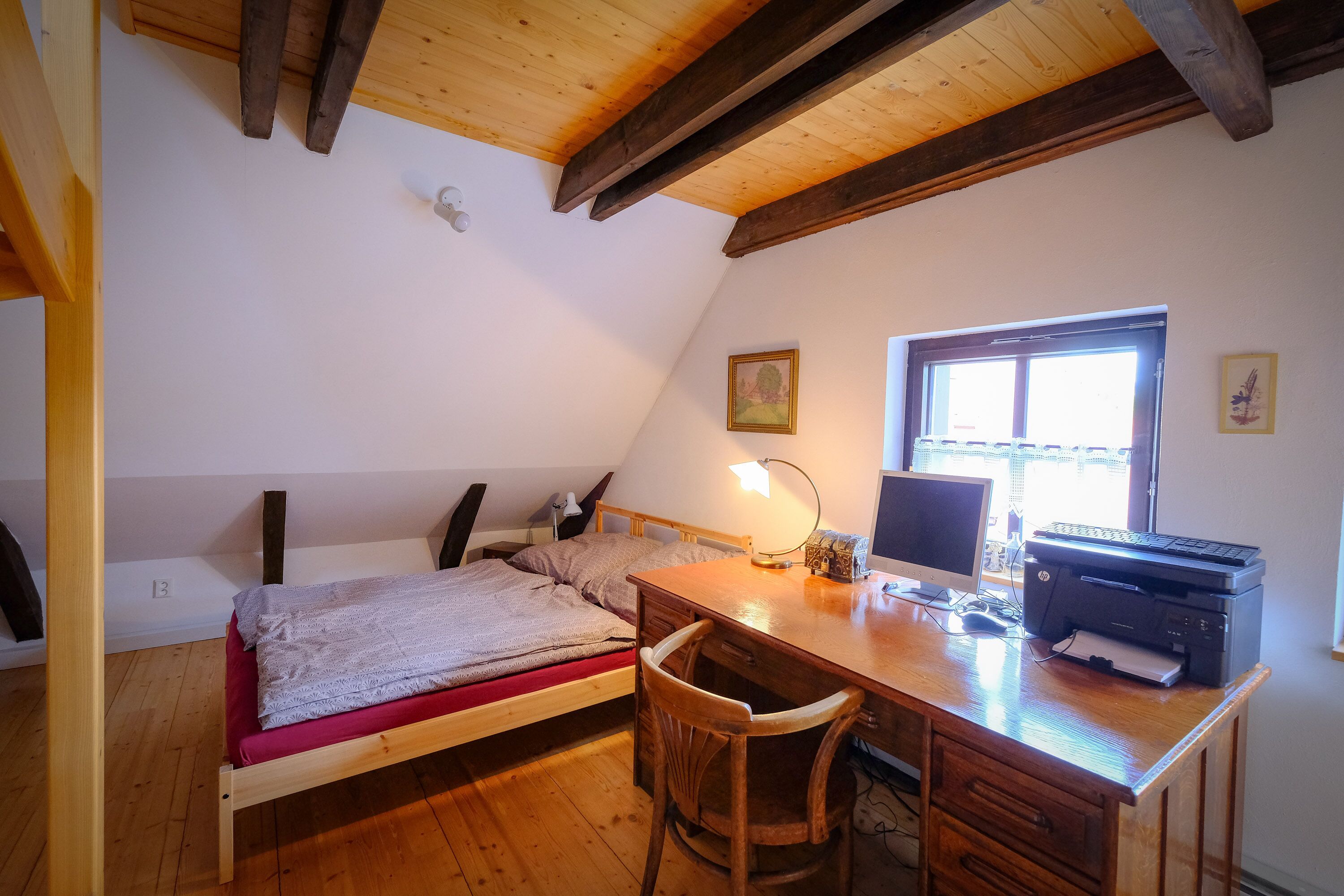 A bedroom with a bed, desk, chair, computer, printer, and window.