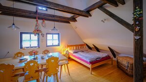 A cozy attic bedroom with a wooden bed, a dining table with chairs, and a large window. - Chalupa na Fryšavě (Frysava pod Zakovou horou)