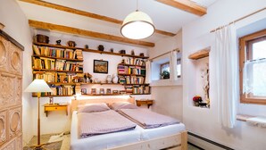 A cozy bedroom with a wooden bed, bookshelves filled with books, a lamp, and a window with curtains. - Chalupa na Fryšavě (Frysava pod Zakovou horou)