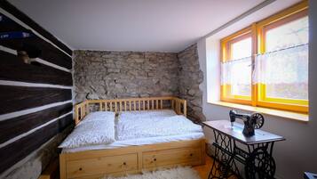 Une chambre avec un lit en bois, un mur en pierre et une machine à coudre près d’une fenêtre.