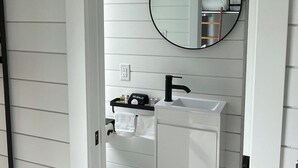 A bathroom with a white vanity, a round mirror, and a black faucet. - Depot Village (Gainesville)