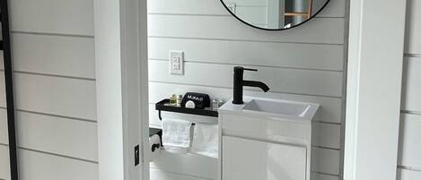 A bathroom with a white vanity, a round mirror, and a black faucet.