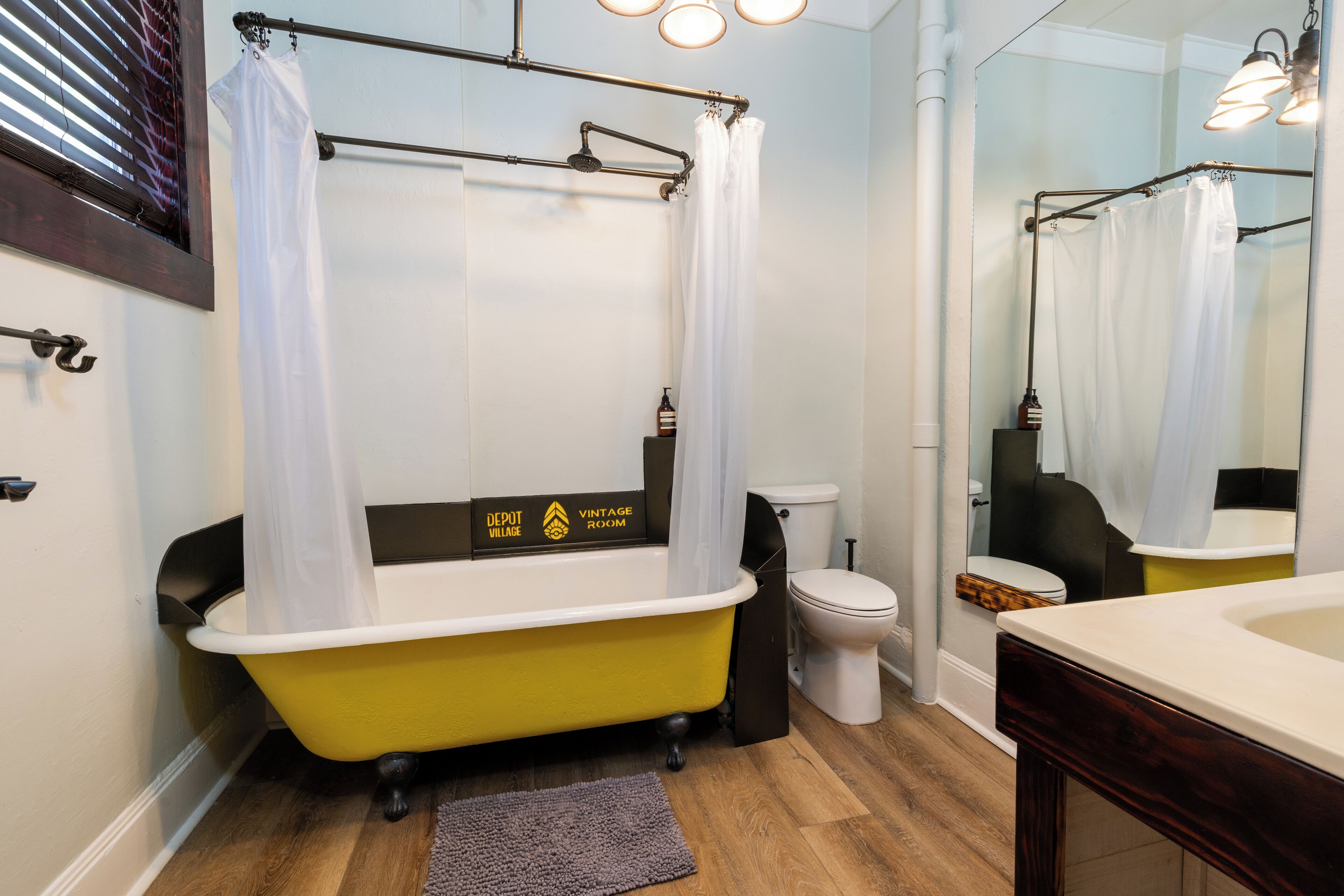Een badkamer met een geel pootbad, een wit toilet en een spiegel die de douche weerkaatst.