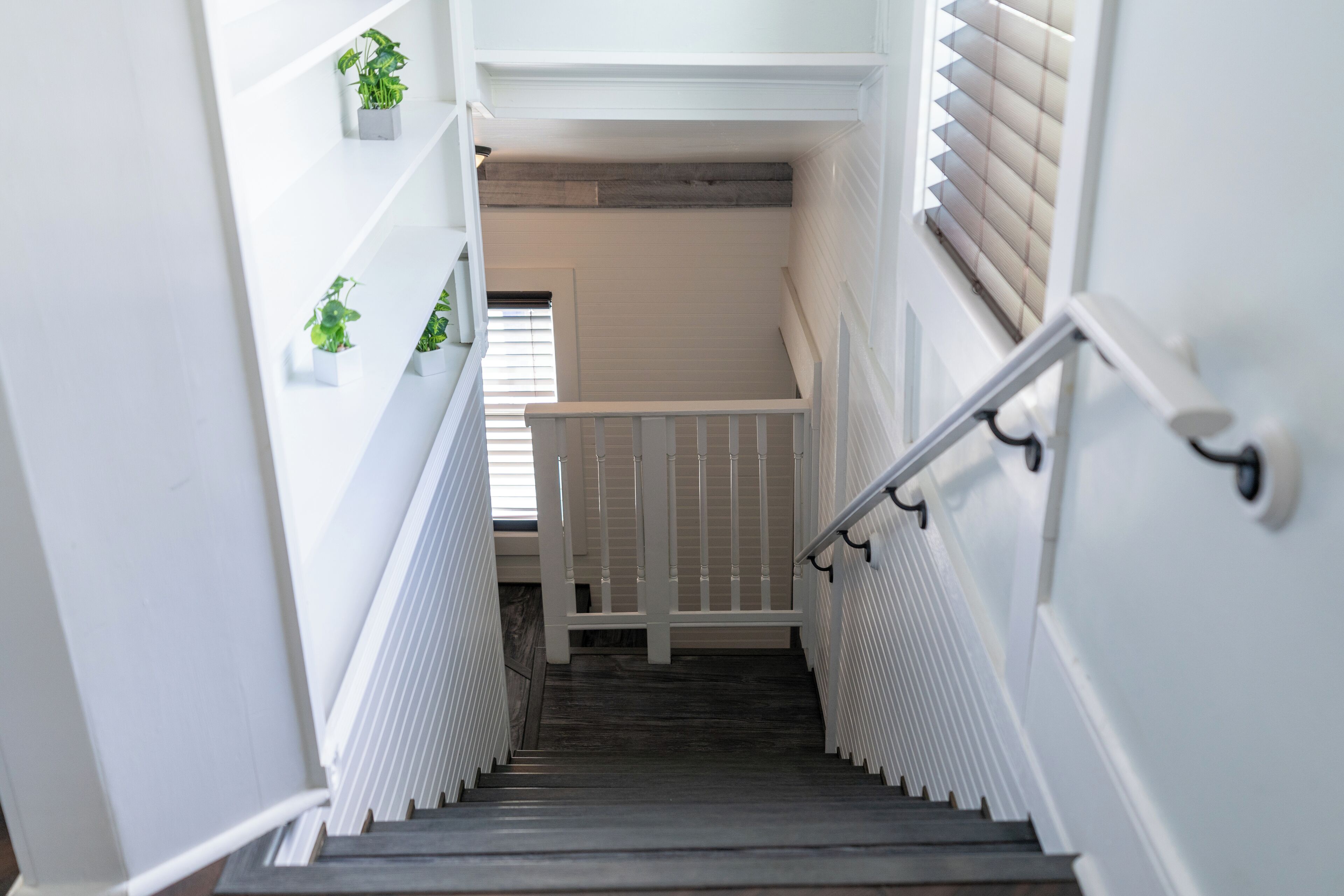 Una escalera con barandillas blancas, suelo de madera y plantas en macetas en las paredes.