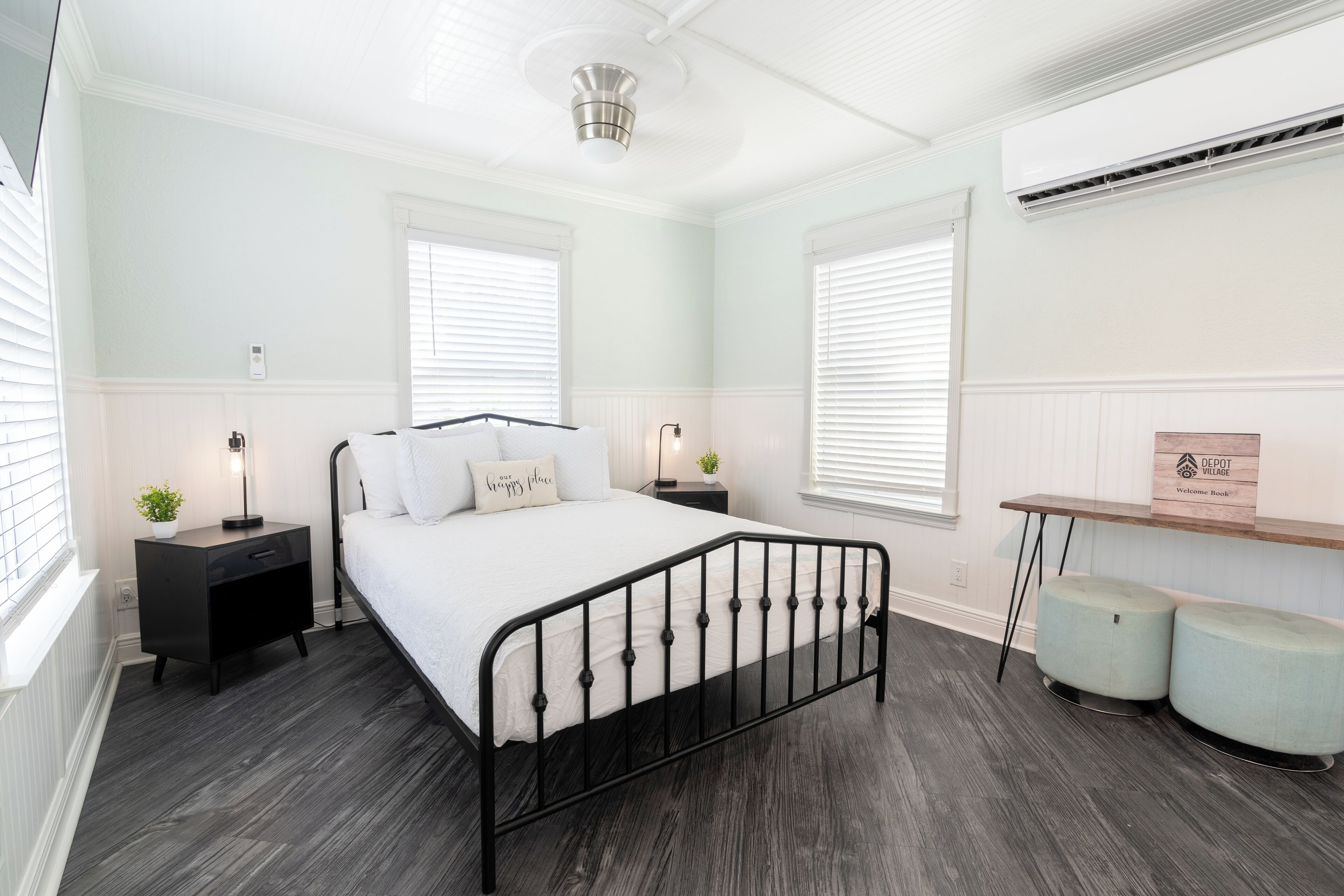 Une chambre à coucher comprenant un lit, deux tables de chevet, une commode, un climatiseur fixé au mur et une petite étagère en bois.