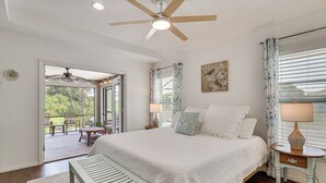 A bedroom with a bed, a ceiling fan, a nightstand, a lamp, a bench, and a view of an outdoor patio. - Fairways & MLB Fun! Poolside Haven in Lehigh Acres (Lehigh Acres)