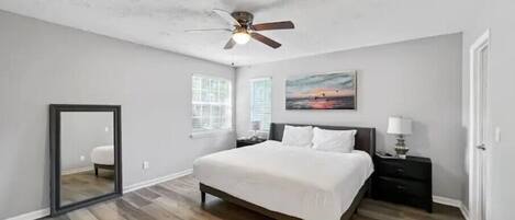A spacious bedroom with a large bed, a ceiling fan, a nightstand with a lamp, and a painting on the wall.