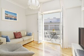 A modern living room with a sofa, a TV, and a balcony with outdoor furniture.