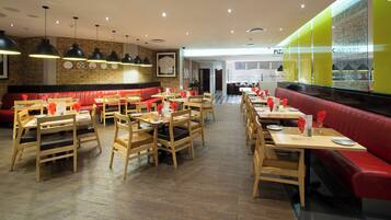 A restaurant with wooden tables and red upholstered booths, featuring a brick wall and pendant lighting.