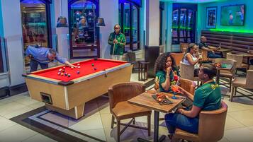 A pool table in a room with multiple seating areas and a television screen.