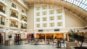 A spacious atrium with multiple levels, featuring a central open area with tables and chairs, surrounded by balconies and shops. - The Ridge Hotel (Emalahleni)