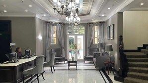 A hotel lobby with a reception desk, seating area, chandelier, and a staircase. - The Ridge Hotel (Emalahleni)