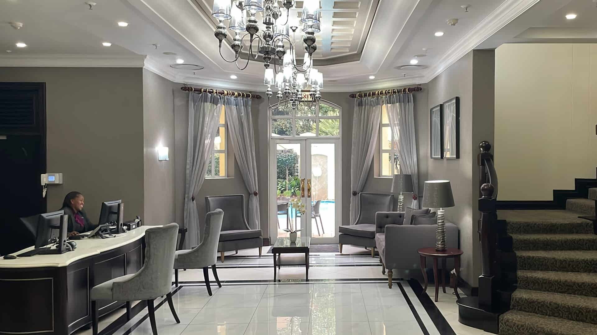 Rebedor d'hotel amb taulell de recepció, zona de seients, un lampadari i una escala.
