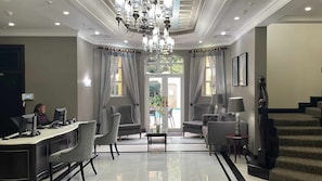 A hotel lobby with a reception desk, seating area, chandelier, and a staircase.