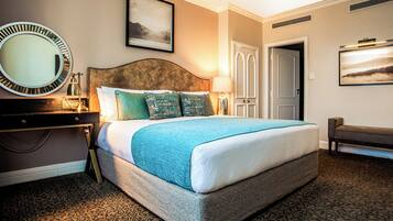 Habitación de hotel con una cama grande, un espejo redondo, una mesita de noche, una lámpara, un banco y una puerta.