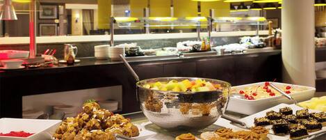 A buffet with various food items including a large bowl of fruit salad, pastries, and desserts.