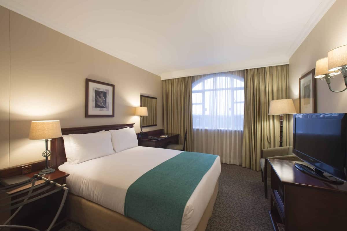 A hotel room with a large bed, two bedside lamps, a television, a desk, and a window with curtains.