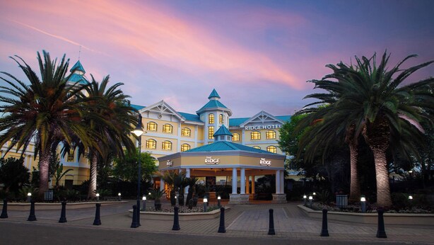 A hotel with a central pavilion, palm trees, and a blue-roofed building. - The Ridge Hotel (Emalahleni)