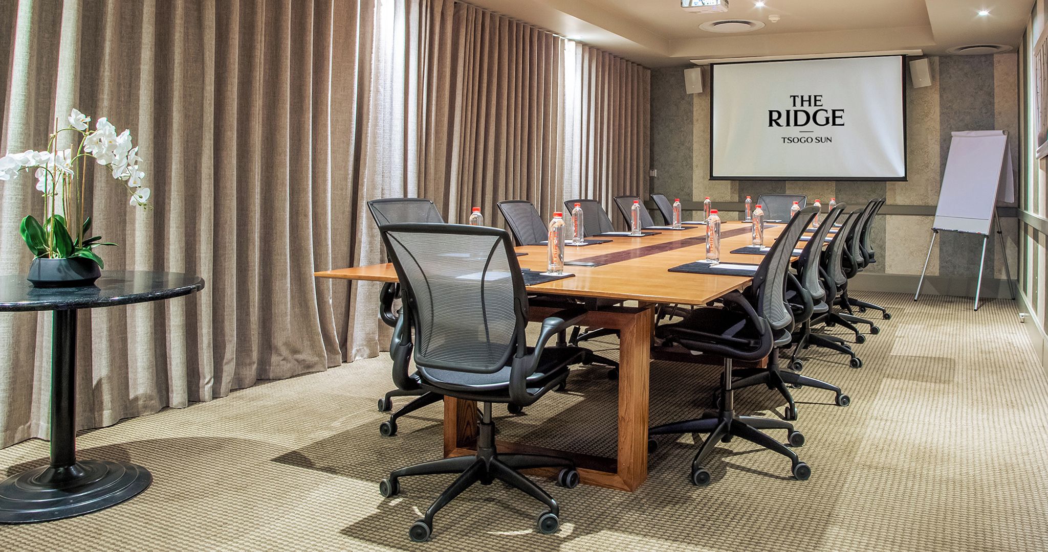 A conference room with a long table, chairs, a projector screen, and a whiteboard.