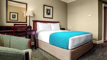 A hotel room with a bed, a desk, a chair, and a lamp.