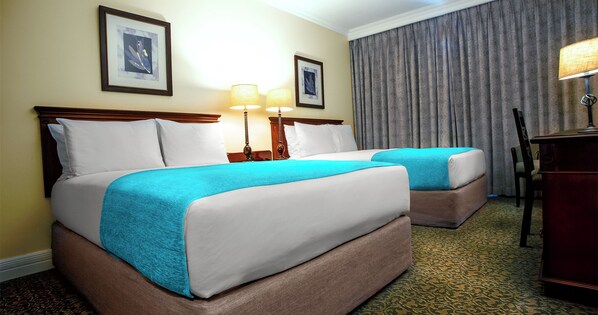 A hotel room with two beds, a desk, a chair, and two lamps.