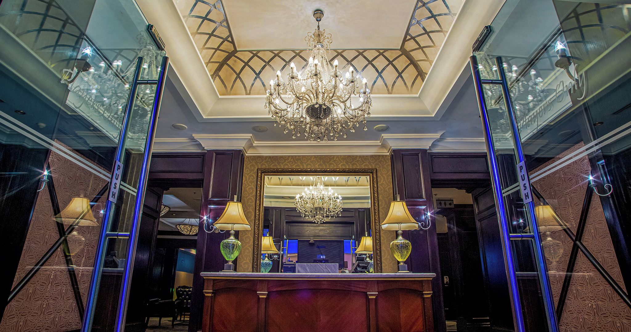 A grand lobby with a large chandelier, a reception desk, and a mirrored wall.