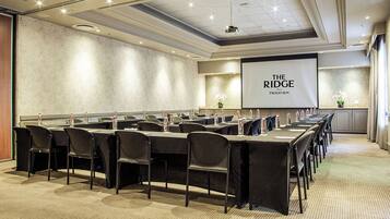 A conference room with a long table, chairs, and a projector screen displaying "THE RIDGE TSOGO SUN".