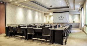 A conference room with a long table, chairs, and a projector screen displaying "THE RIDGE TSOGO SUN".