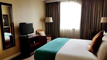A hotel room with a bed, a television, a chair, and a window with curtains.