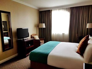 A hotel room with a bed, a television, a chair, and a window with curtains.