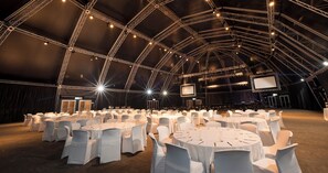 A large indoor event space with multiple round tables covered with white tablecloths and white chairs. - The Ridge Hotel (Emalahleni)