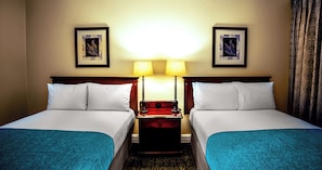 A hotel room with two single beds, a nightstand with lamps, and framed artwork on the walls.
