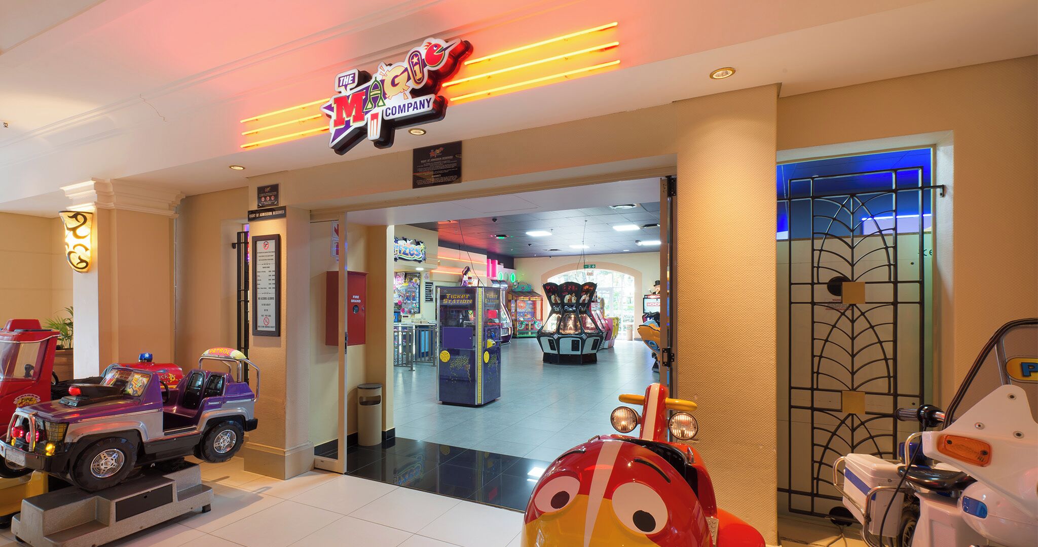 A brightly lit arcade area with various gaming machines and a neon sign for 'The Magic Company'.