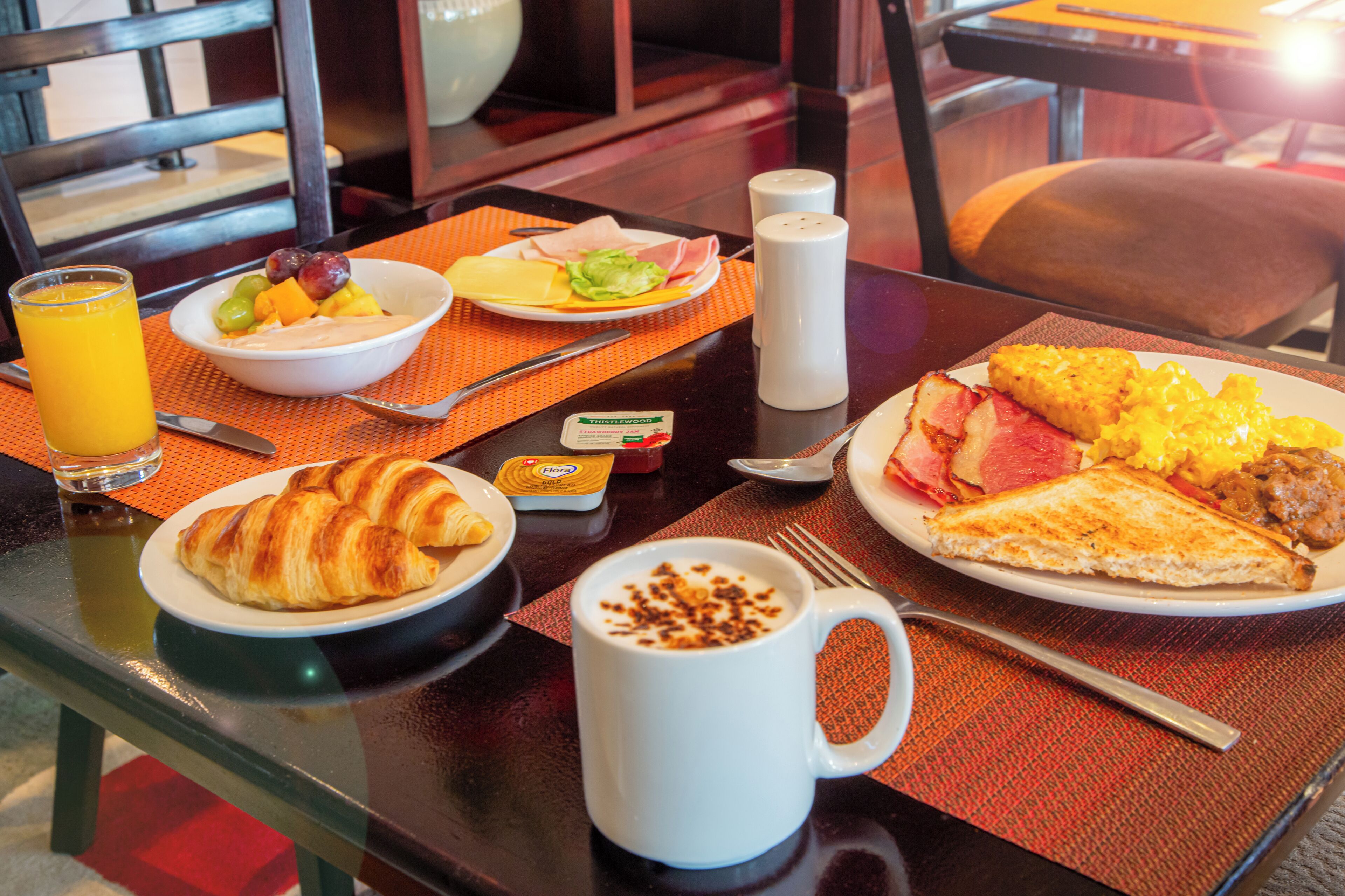 A breakfast table with croissants, a bowl of fruit, scrambled eggs, and a coffee mug.