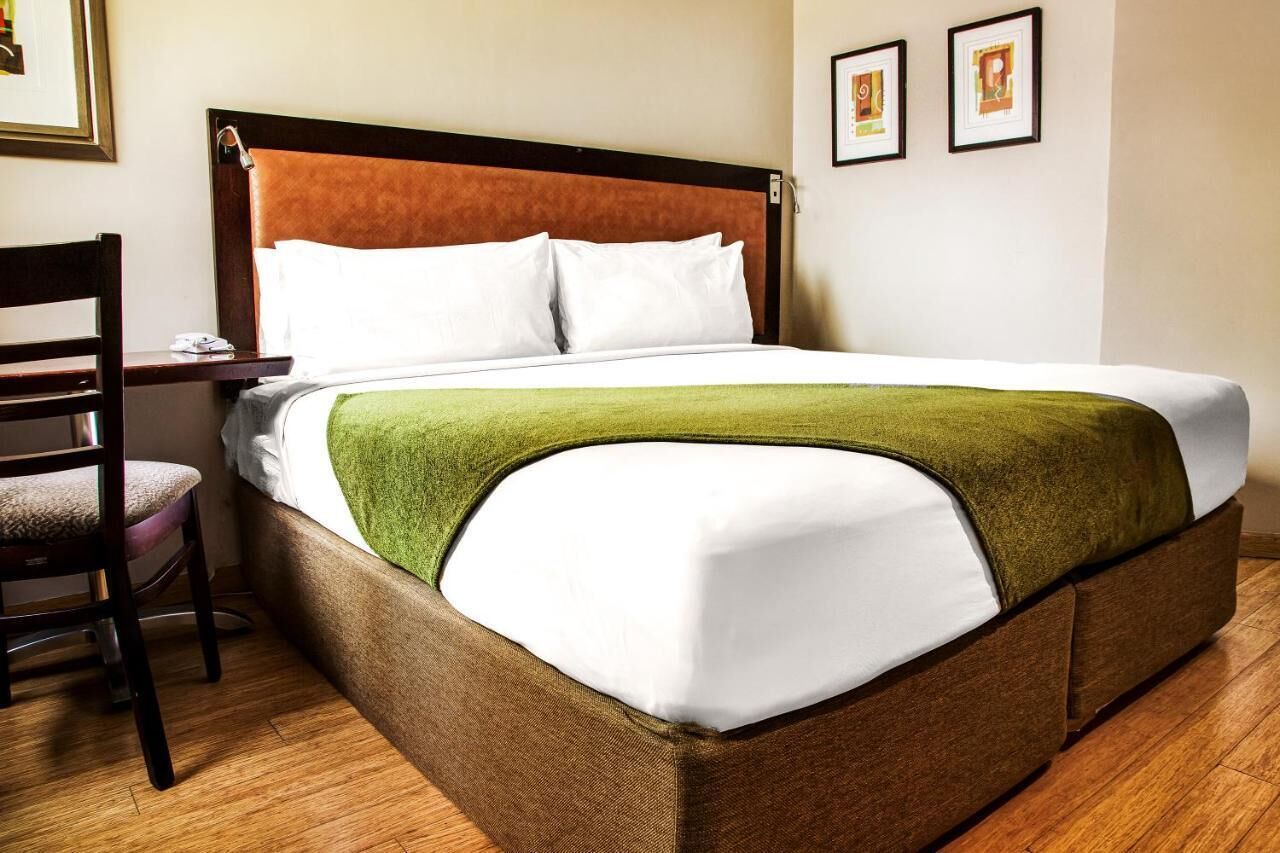 A neatly made bed with a green throw blanket, a wooden headboard, and a wooden chair beside it.