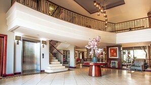 A spacious lobby with a high ceiling, a staircase, and a large seating area. - The RidgePoint Hotel (Emalahleni)