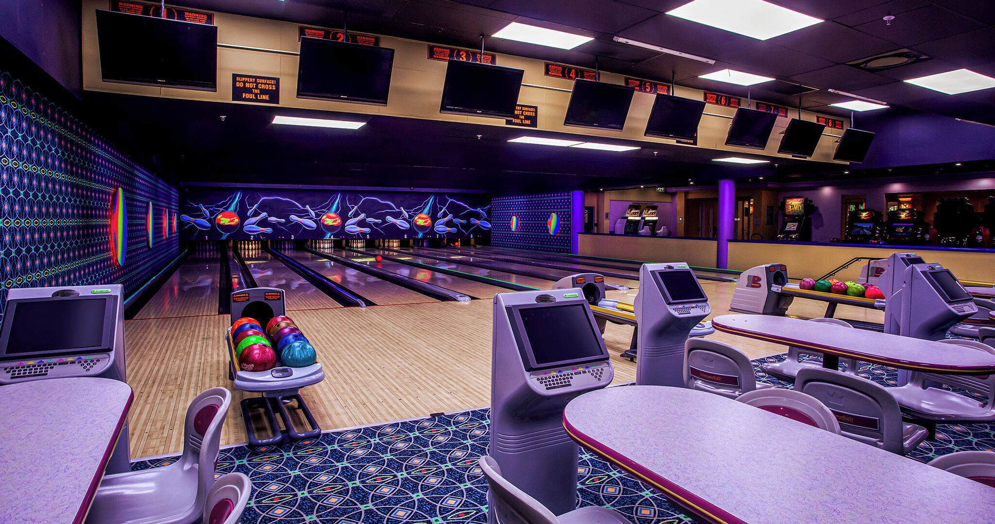 A bowling alley with multiple lanes, bowling balls, and electronic scoreboards.