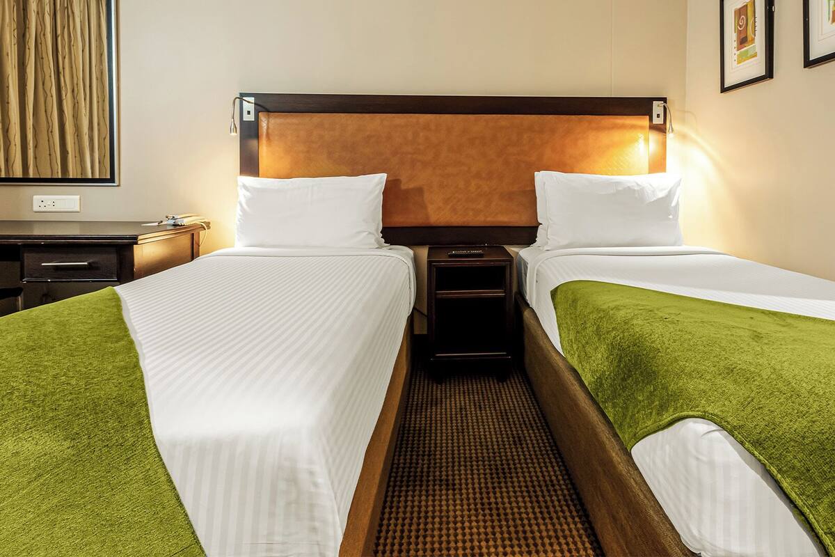 A hotel room with two single beds, a wooden headboard, a nightstand, and a desk with a chair.