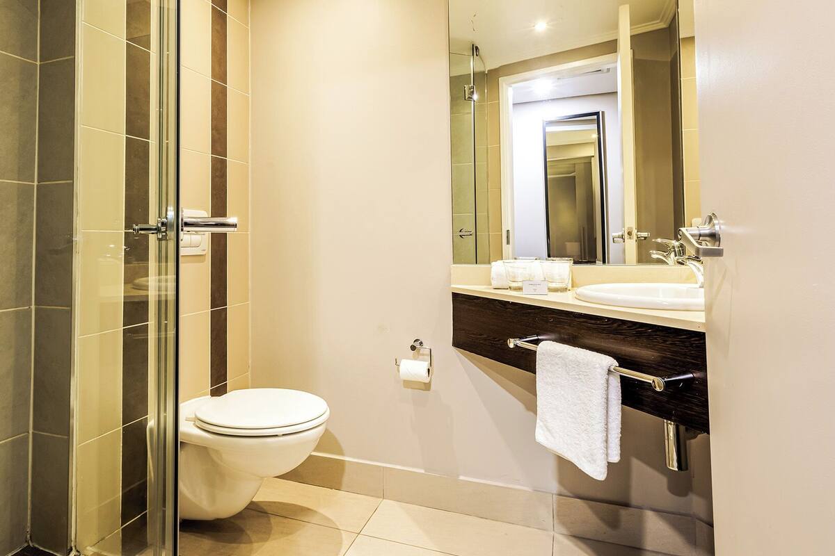A modern bathroom with a glass-enclosed shower, a white toilet, a vanity with a mirror, and a towel rack.