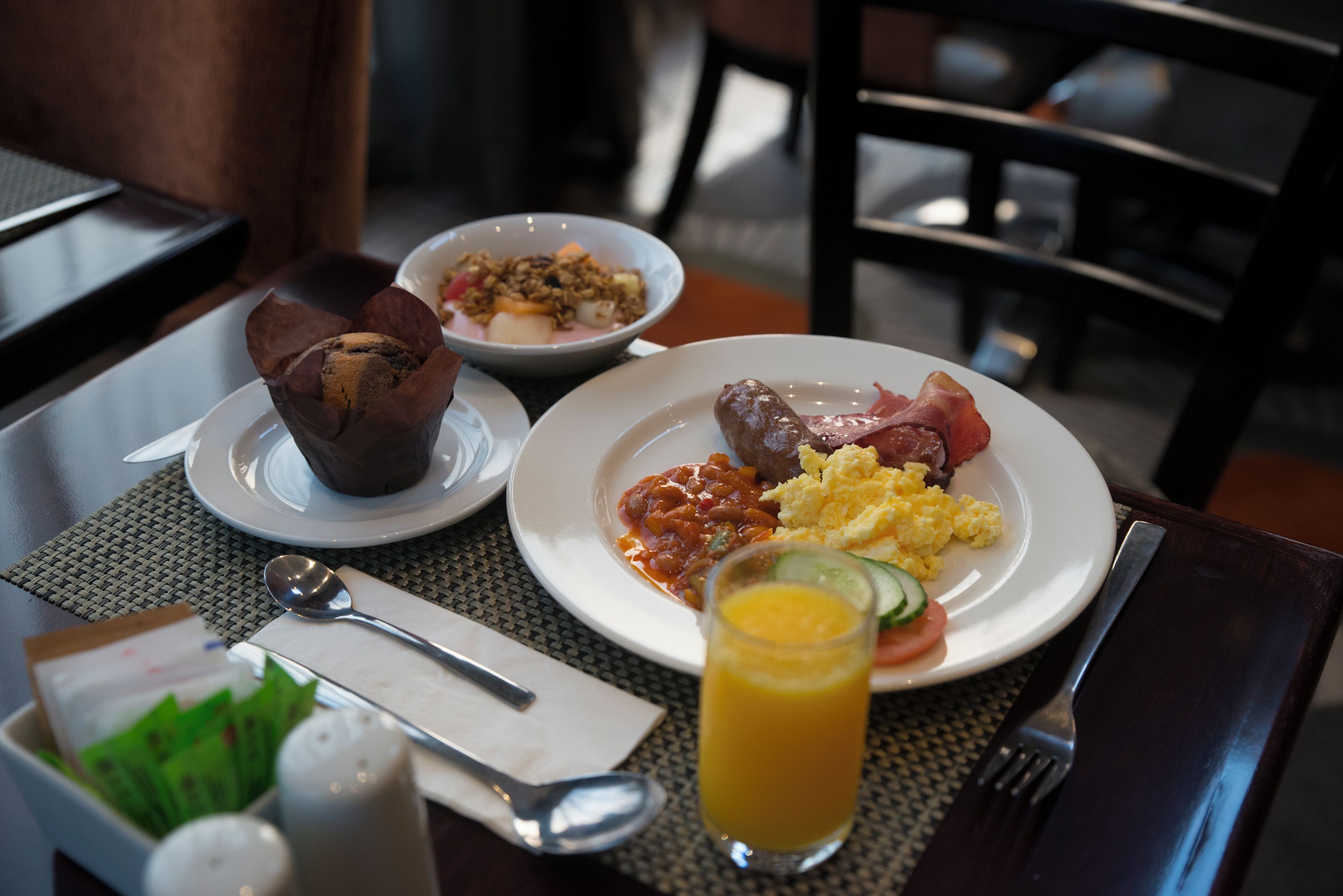 A breakfast setting with plates of food, a glass of orange juice, and a bowl of cereal.