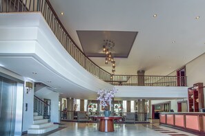 Eine geräumige Lobby mit einer zentral platzierten Blumenkomposition, einer Treppe und einem Empfangsbereich.