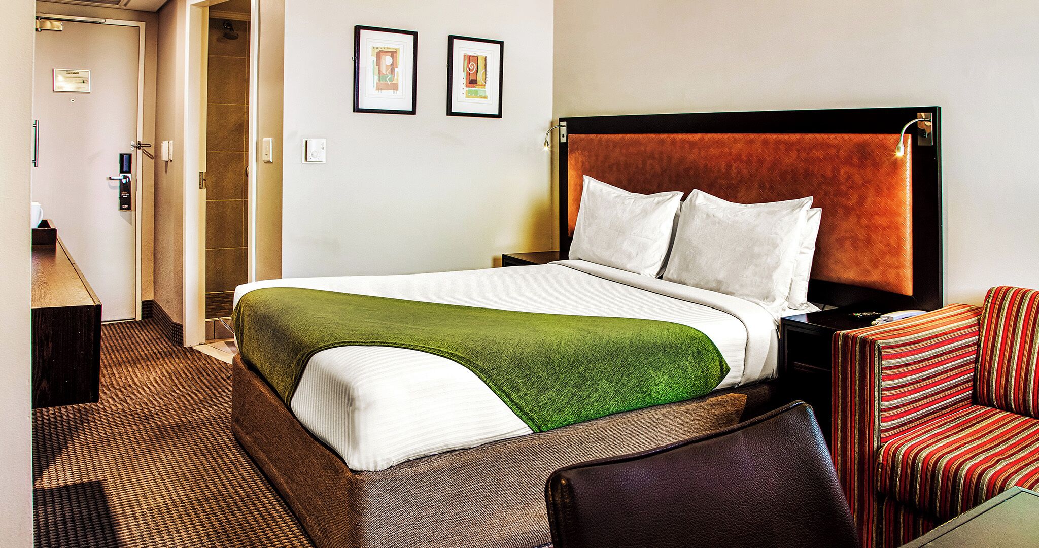 Ein Hotelzimmer mit Bett, einer grünen Decke, einem gestreiften Sessel und einem Fernseher.