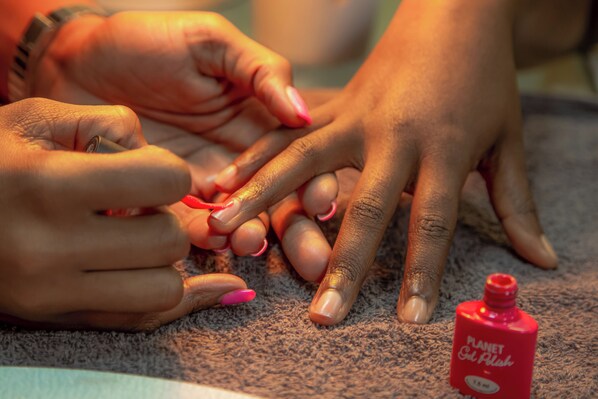 Een close-up van handen met roze nagellak, een fles Planet Oil Polish en een horloge om een pols.