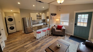 Una cocina moderna con una isla central, un comedor con una mesa de centro y una sala de estar con sofá y televisor.