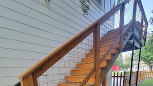 Una escalera de madera con barandilla de metal que lleva a un porche cubierto.