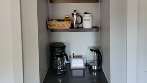 Una encimera de cocina con una cafetera, un hervidor y un cuadro enmarcado encima.