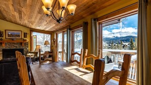 A spacious room with a large wooden table, comfortable seating, a fireplace, and large windows offering a mountain view.