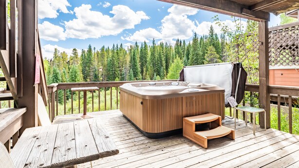 A wooden deck with a hot tub, wooden benches, and a view of a forest.